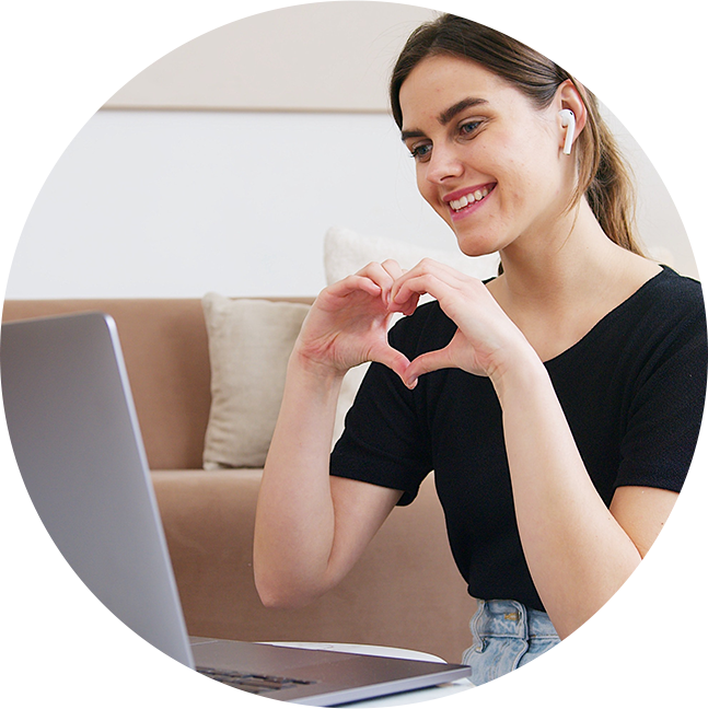 Girl making heart symbol with hands while talking on computer.